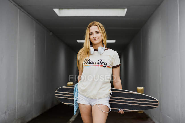Blondes Mädchen mit Longboard im Lampenlicht — Stockfoto