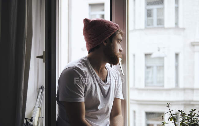 Hombre reflexivo sentado en el alféizar de la ventana - foto de stock