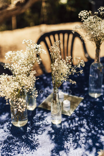 Маленькие белые деревенские цветы в бутылках вина на столе. — стоковое фото
