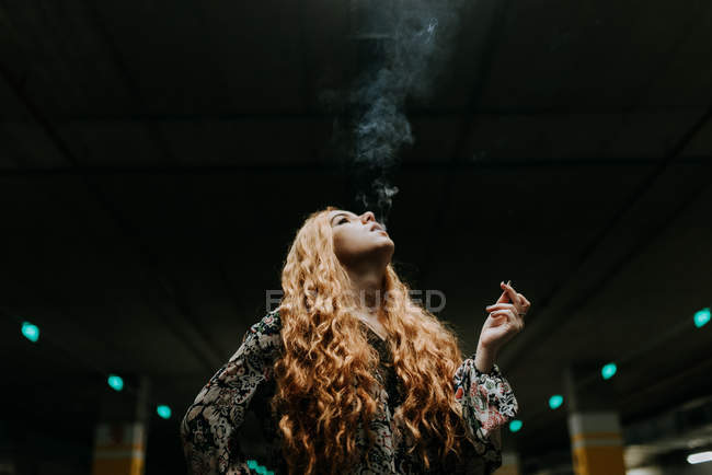 Jolie rousse femme fumant sur un parking flou — Photo de stock