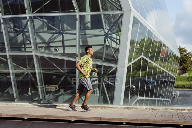 Uomo etnico che fa jogging contro l'edificio moderno in città — Foto stock