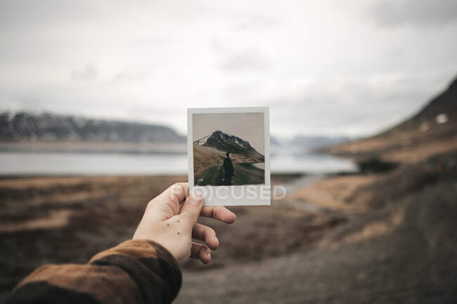 Mão de colheita segurando tiro instantâneo com turista e colina no lago na Islândia. — Fotografia de Stock