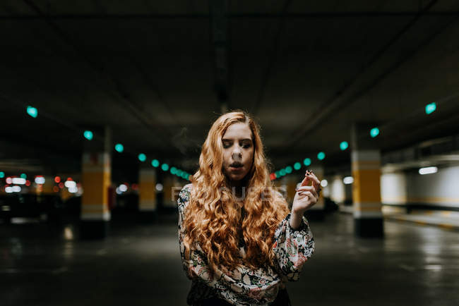 Redhead woman with eyes closed smoking on blurred parking lot — Stock Photo
