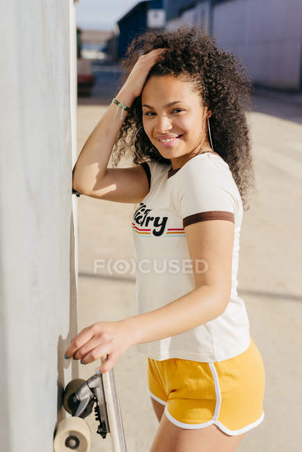Teenage girl with skateboard standing at wall — Stock Photo