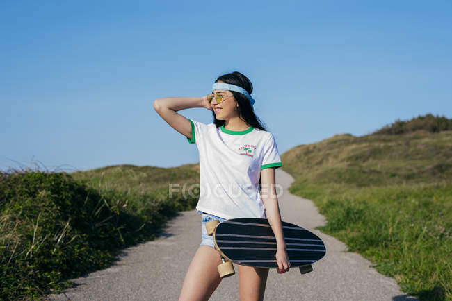 Chica con longboard de pie en el camino - foto de stock