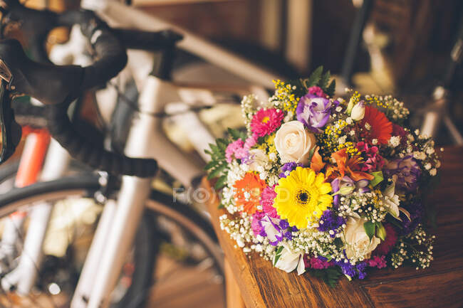 Bando de diferentes flores coloridas na mesa e bicicleta esportiva dentro de casa. — Fotografia de Stock