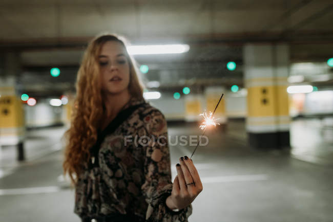Young woman standing on parking lot with sparkler — Stock Photo
