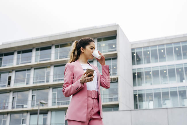 Mujer en traje rosa con café y teléfono inteligente - foto de stock