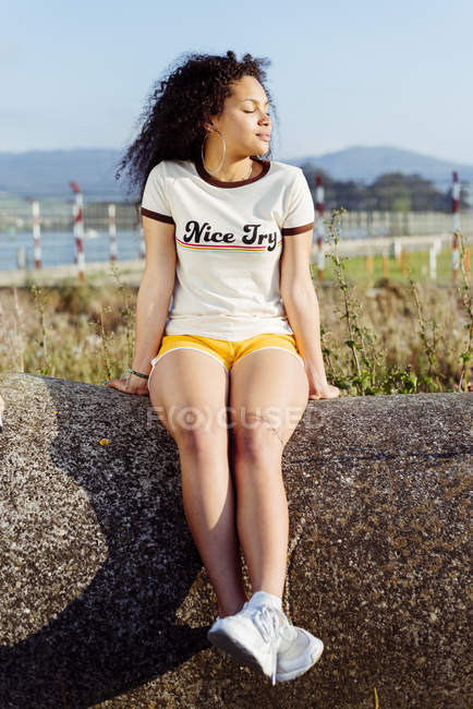 Девочка-подросток, сидящая на скале на берегу — стоковое фото