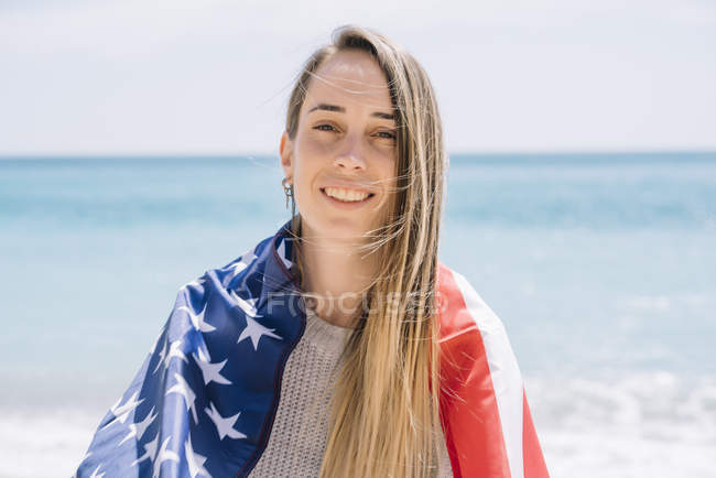 Porträt einer jungen Frau, die mit US-Flagge am Strand posiert. — Stockfoto