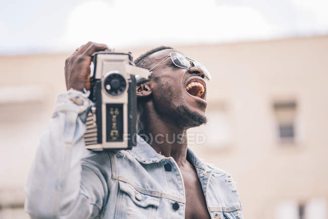 Smiling black man in sunglasses walking with vintage radio device and singing — Stock Photo