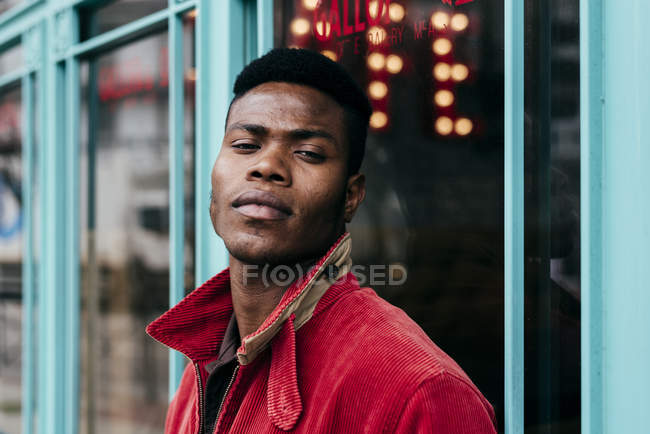 Hombre de chaqueta roja de pie contra la cafetería - foto de stock