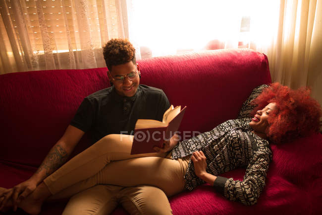 Homem leitura livro com namorada no sofá — Fotografia de Stock