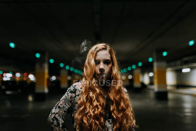 Mulher ruiva grave fumar no estacionamento turvo — Fotografia de Stock