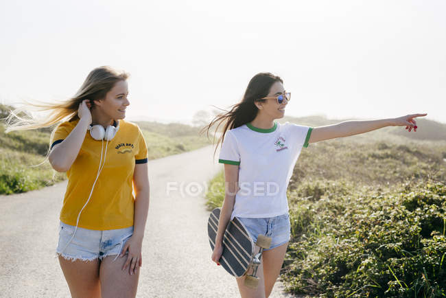 Girls with longboard walking on road — Stock Photo