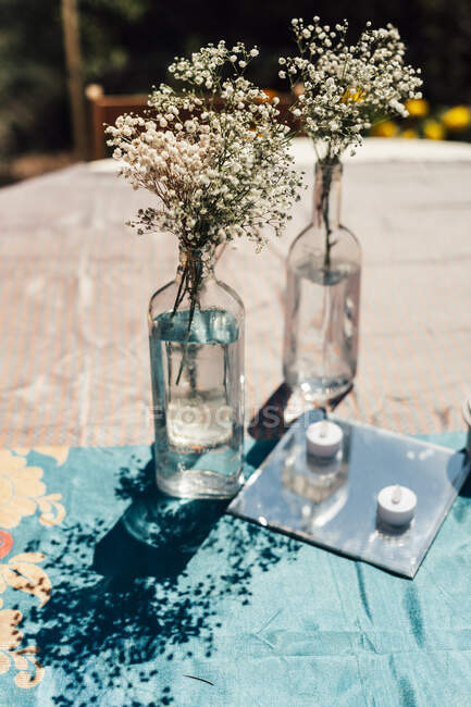 Pequeñas flores rústicas blancas en botellas de vino sobre la mesa. - foto de stock