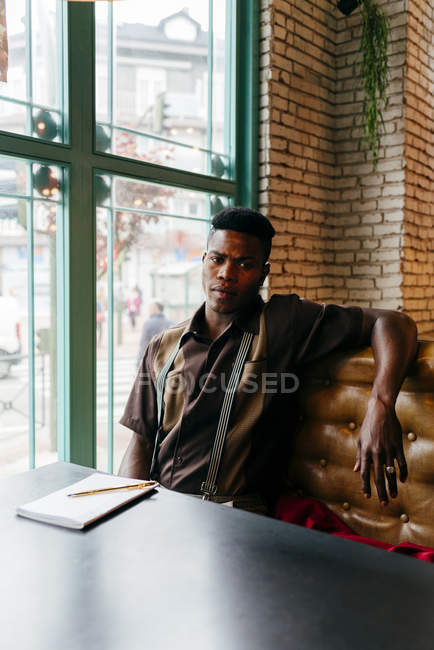 Hombre negro sentado en la mesa en la cafetería - foto de stock