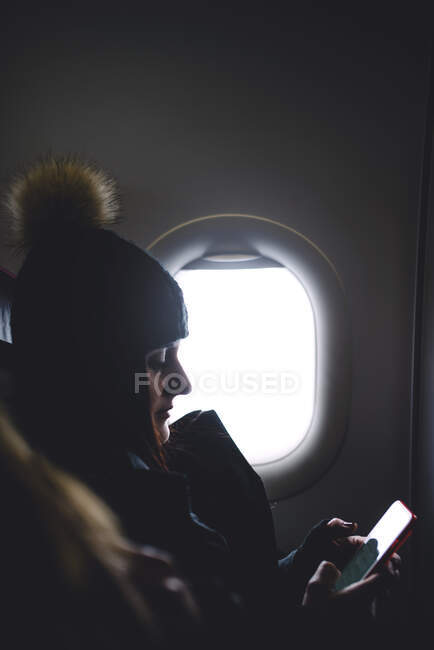 Pretty woman looks at the mobile phone sitting in airplane window. — Stock Photo