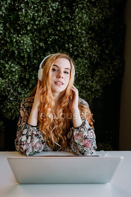 Fröhliche hübsche rothaarige Frau sitzt am Laptop und tippt am Tisch. — Stockfoto