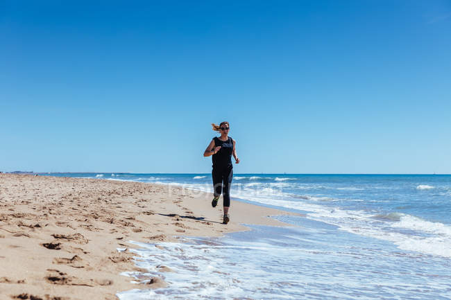 Donna che corre lungo la spiaggia di sabbia — Foto stock
