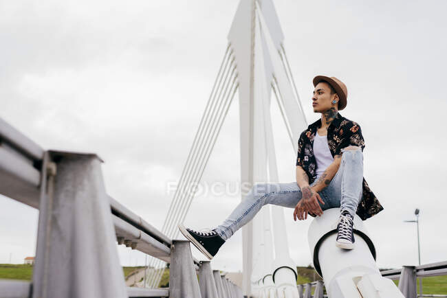 Hipster sitting on railing of bridge — Stock Photo