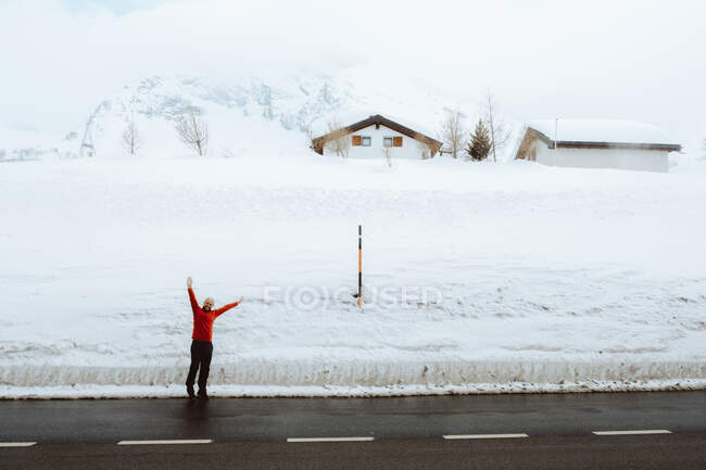 Взрослый мужчина, стоящий с поднятыми руками на асфальтовой дороге в зимний день, Simplon Pass, Швейцария / Италия — стоковое фото