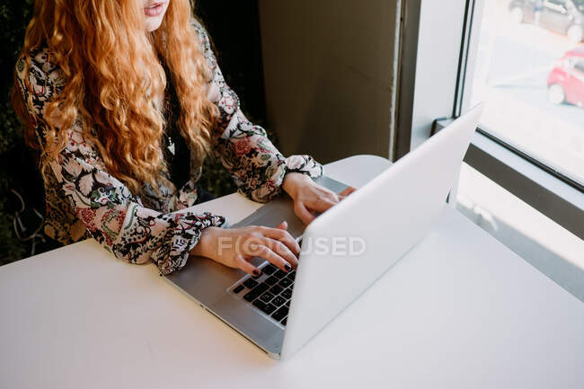 Весела красива руда жінка сидить на ноутбуці і друкує за столом . — стокове фото
