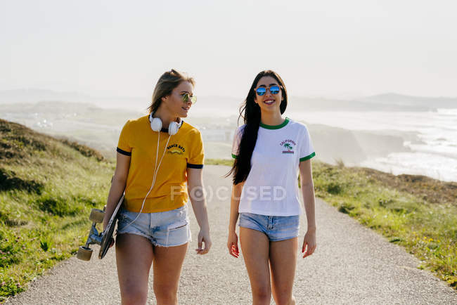 Девушки-подростки с длинной доской прогулки по дороге — стоковое фото