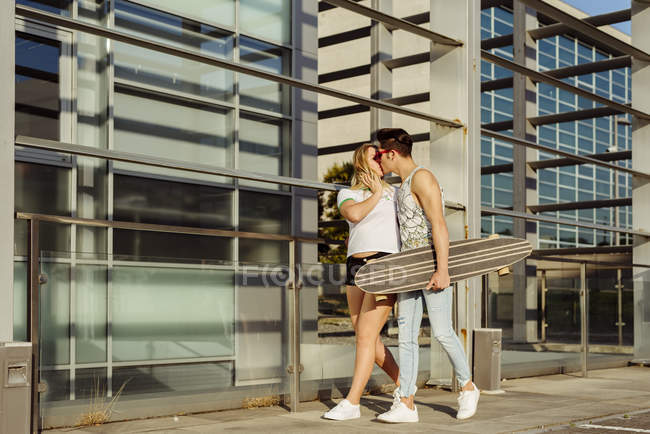 Couple avec skateboard baisers dans la rue — Photo de stock