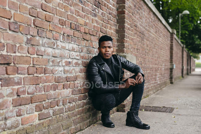 Homme noir accroupi contre un mur de briques — Photo de stock