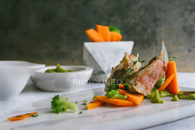 Grilled scorpion fish with mashed peas and carrot sticks on marble plate — Stock Photo