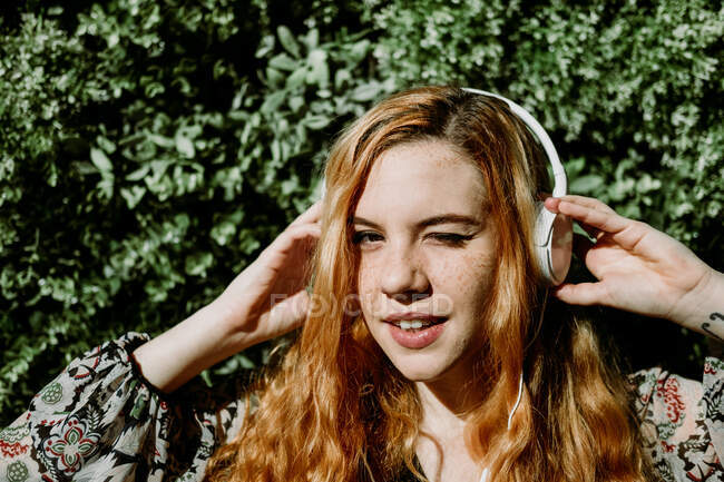 Pretty young redhead woman putting on headphones at the bush. — Stock Photo