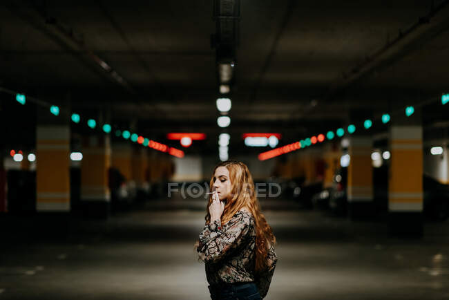 Pretty redhead woman having smoke on blurred parking lot. — Stock Photo