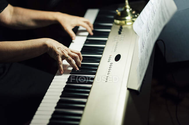 Vista lateral de las manos de los cultivos de músico sentado y tocando el piano eléctrico. - foto de stock