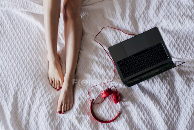 Gambe femminili e laptop con cuffie — Foto stock