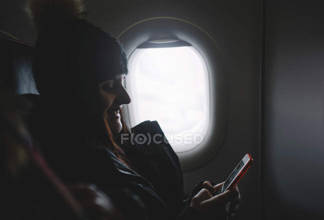 Bella donna guarda il telefono cellulare seduto in finestra aereo
. — Foto stock
