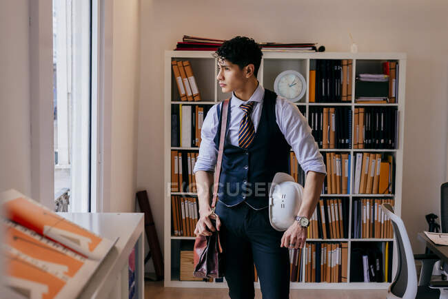 Schöner junger asiatischer Mann steht im Büro und schaut weg. — Stockfoto