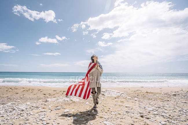 Young woman walking with USA flag on sandy beach. — Stock Photo