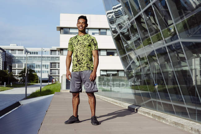 Schöner sportlicher ethnischer Mann steht in der Stadt mit modernen Gebäuden im Hintergrund — Stockfoto