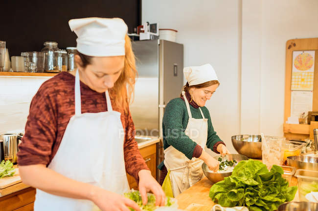 Women working with lettuce in kitchen — Stock Photo