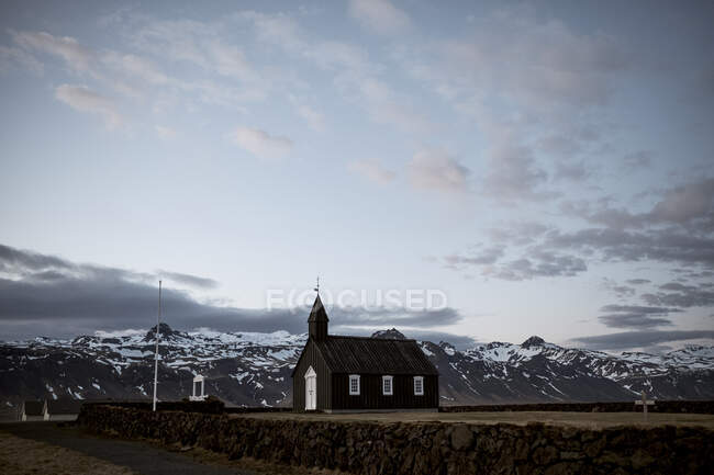 Piccolo edificio chiesa nera posto sul campo a montagne innevate in Islanda — Foto stock