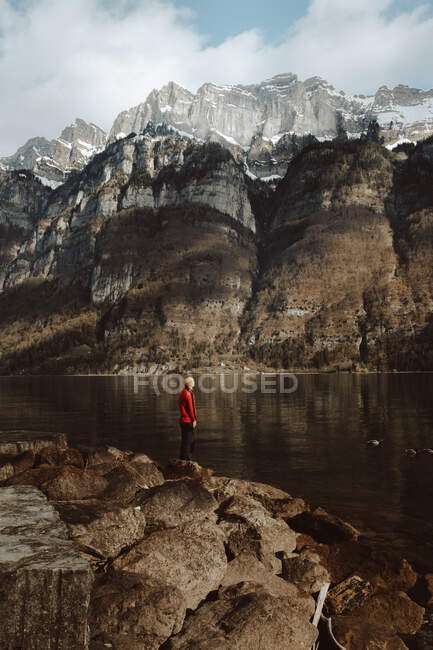 Vue latérale d'un touriste adulte debout au bord d'un lac calme dans les montagnes, Walensee, Suisse — Photo de stock