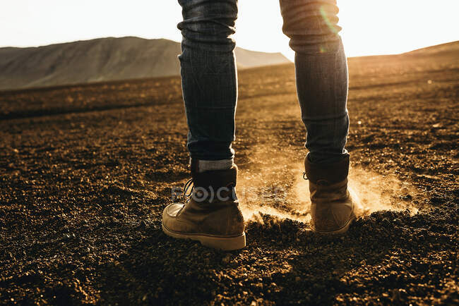 Legs of unrecognizable tourist standing on dry ground in hillside in sunset lights. — Stock Photo