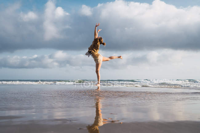Chica haciendo ejercicios en la playa con cielo nublado en el fondo - foto de stock