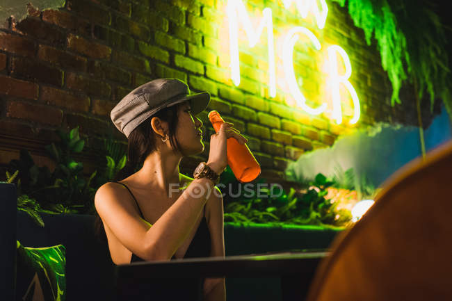 Elegante jovem mulher asiática sentada no café e tendo garrafa de bebida — Fotografia de Stock