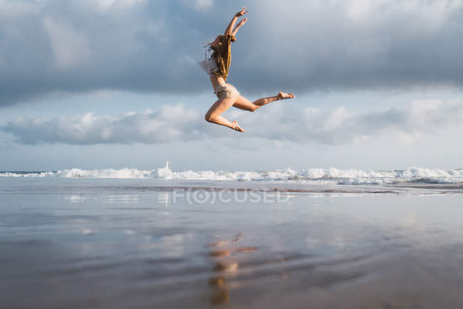 Girl jumping on beach with cloudy sky on background — Stock Photo
