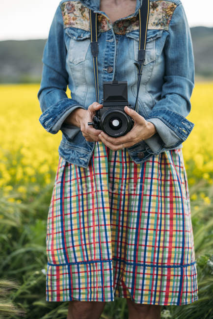 Жінка в кольоровій сукні і джинсовій куртці, що тримає фото пристрій в природі — стокове фото