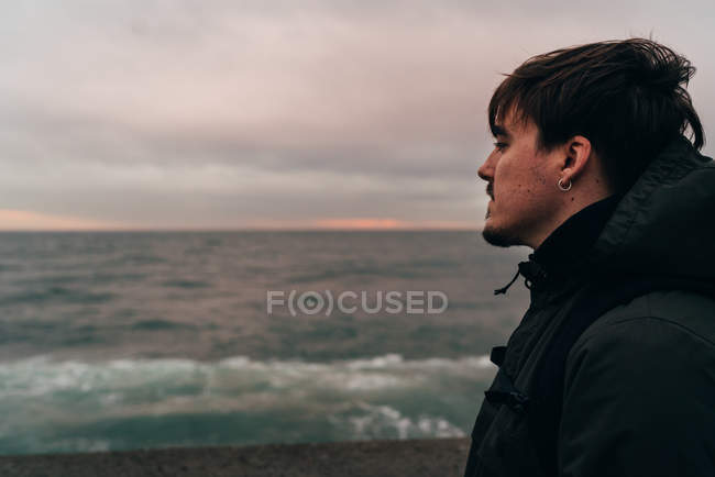 Homem pensativo em pé no mar em nublado e olhando para longe — Fotografia de Stock