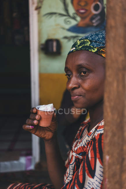 Kamerun - Afrika - 5. April 2018: Ethnische Frau lehnt an Wand und hält Plastikglas — Stockfoto