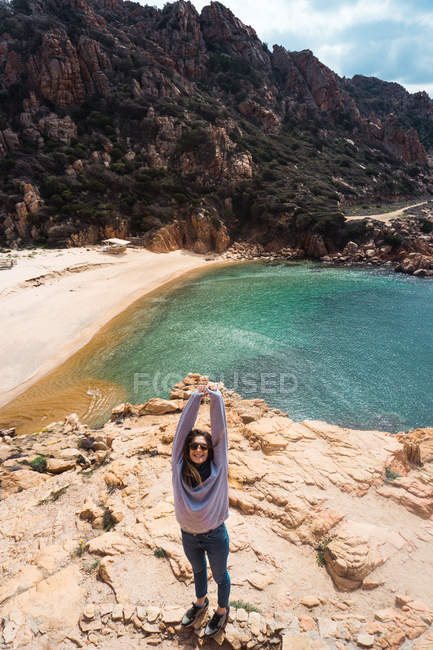 Donna sorridente in piedi al mare con le braccia alzate — Foto stock